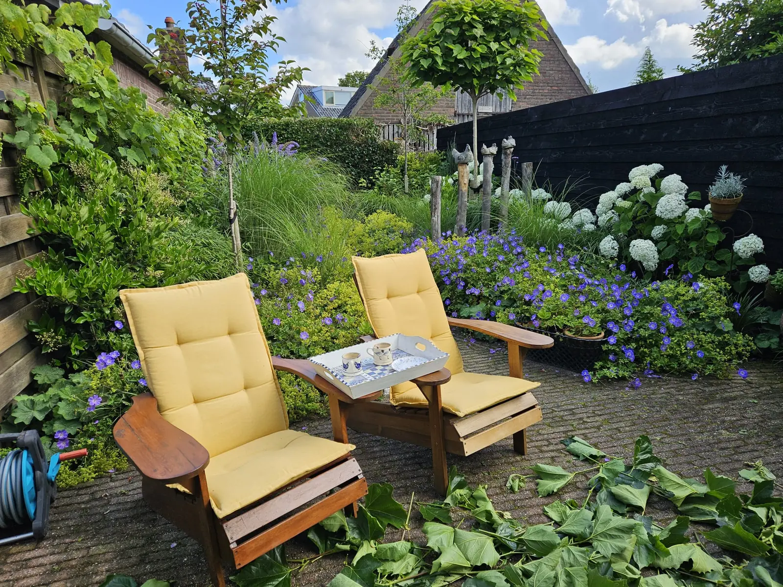 Terras met klinkers, tuinstoelen en bloeiende borders